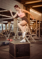 Fit woman in sportswear steps on wooden box in the gym. Intensive functional training