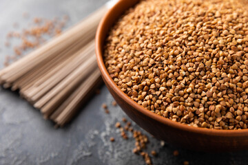 Buckwheat porridge in a bowl and sobo noodles on a black textured marble background. Raw buckwheat. Ingredients for gluten free cereal. Healthy food. Place to copy.