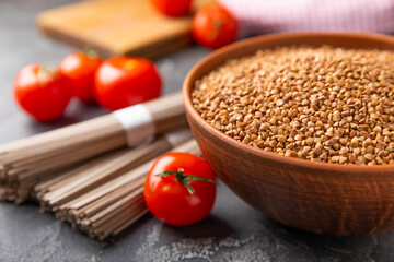 Buckwheat in a bowl with cherry tomatoes and buckwheat soba noodles on a textured background. raw...