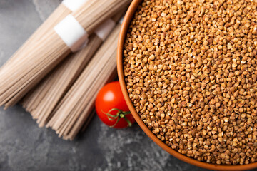 Buckwheat in a bowl with cherry tomatoes and buckwheat soba noodles on a textured background. raw buckwheat. Ingredients for gluten free cereal. Health food. Place to copy.