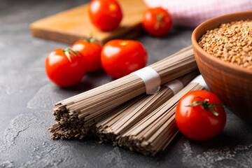 Buckwheat soba paste and cherry tomatoes on a textured background.Raw noodles. Ingredients for a gluten free dish. Dried buckwheat soba noodles. Traditional Japanese food. Healthy food. Place to copy.