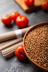 Buckwheat in a bowl with cherry tomatoes and buckwheat soba noodles on a textured background. raw buckwheat. Ingredients for gluten free cereal. Health food. Place to copy.