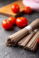Buckwheat soba paste and cherry tomatoes on a textured background.Raw noodles. Ingredients for a gluten free dish. Dried buckwheat soba noodles. Traditional Japanese food. Healthy food. Place to copy.