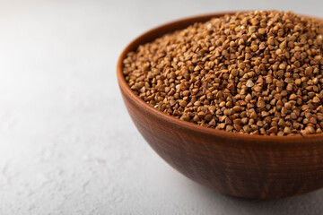Buckwheat in a bowl on a textured background. raw buckwheat. Ingredients for gluten free cereal. Health food. Place to copy.