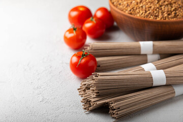 Buckwheat soba paste and cherry tomatoes on a textured background.Raw noodles. Ingredients for a gluten free dish. Dried buckwheat soba noodles. Traditional Japanese food. Healthy food. Place to copy.