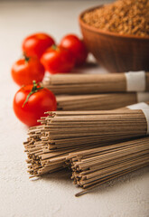 Buckwheat soba paste and cherry tomatoes on a textured background.Raw noodles. Ingredients for a gluten free dish. Dried buckwheat soba noodles. Traditional Japanese food. Healthy food. Place to copy.