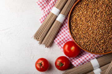 Buckwheat in a bowl with cherry tomatoes and buckwheat soba noodles on a textured background. raw buckwheat. Ingredients for gluten free cereal. Health food. Place to copy.