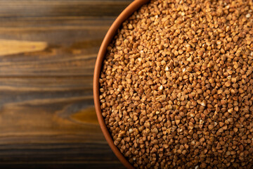 Buckwheat porridge in a bowl on a brown wooden background. Raw buckwheat. Ingredients for gluten free cereal. Healthy food. Place to copy.