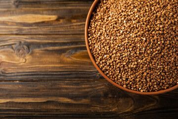 Buckwheat porridge in a bowl on a brown wooden background. Raw buckwheat. Ingredients for gluten free cereal. Healthy food. Place to copy.