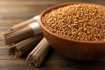 Buckwheat porridge in a bowl and buckwheat soba noodles on a brown wooden background. Raw buckwheat. Ingredients for gluten free cereal. Healthy food. Place to copy.
