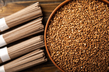 Buckwheat porridge in a bowl and buckwheat soba noodles on a brown wooden background. Raw buckwheat. Ingredients for gluten free cereal. Healthy food. Place to copy.