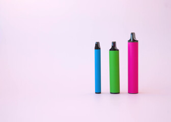 Three electronic cigarettes bright pink green and blue of different sizes on a pink background