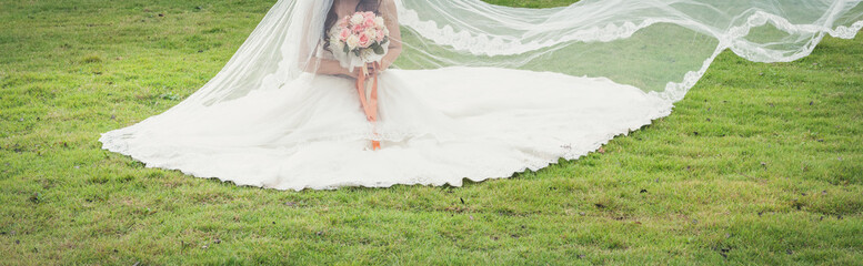 Bride with a bouquet in her hands sitting on the green grass in the park. Concept of bride banner...