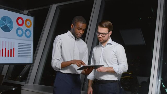 Businessmen using digital tablet together in front of office building windows