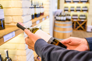 A man choosing and holding a wine bottle in a liquor wine shop. Variations of wine bottles on the...