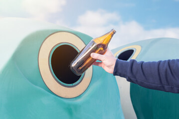 Man recycling glass. Throwing a glass bottle into a green recycling garbage can. Caring for the environment