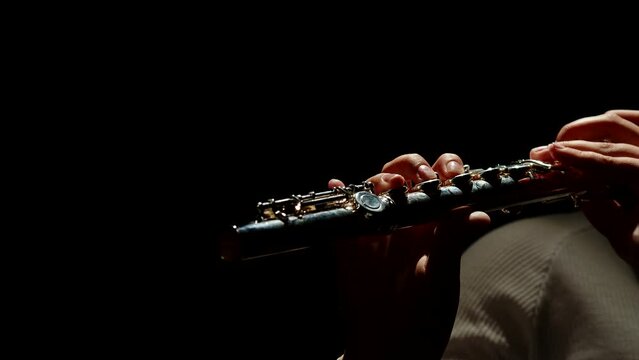 Female fingers playing the flute, close-up. Thin female fingers move on the keys of a chrome flute playing classical music on a black background.