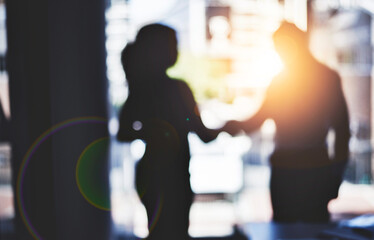 Partnerships are the backbone to strengthening business. Defocused shot of two businesspeople shaking hands in an office.