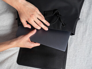 Close-up of a woman's hand putting a gray laptop in a black bag, the concept of working from home,...