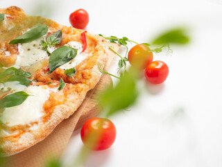 Close-up of a delicious Roman pizza with vegetables on a white background. ripe red tomatoes and micro-greens lie nearby. Traditional Italian food. Side view, selective focus.