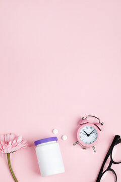 women health concept. medicine, health care style. copy space. white plastic bottle with pills, flowers, glasses and clock on pink background. 