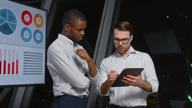 Two colleagues discussing a business project using a digital tablet near the screen in the workplace
