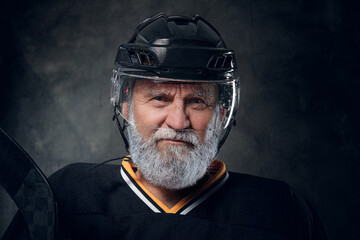 Headshot of senior man hockey player dressed in black sportswear and helmet holding hockey stick.