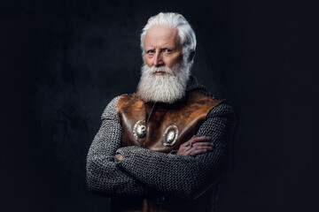Shot of gray haired medieval soldier dressed in armored clothes posing against dark background.