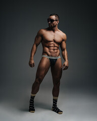 Fototapeta na wymiar Naked sportsman in sunglasses standing in studio