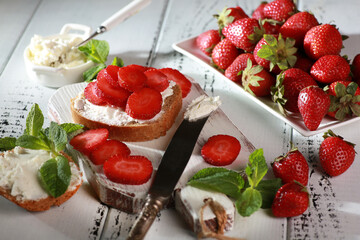 Summer season. Sandwiches with strawberries and cream cheese, mint on white plates on a white...