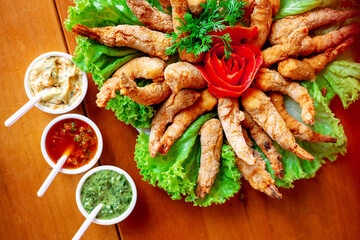 battered and fried shrimp on a large plate decorated with tomato and lettuce, accompanied by various sauces