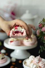 Hand holding a sliced pink meringue dessert revealing berry filling, with elegant table setup.
