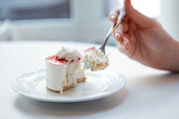 Red and white cake being cut with fork in female hand.