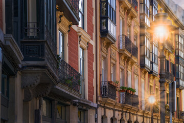 Zabytkowa fasada budynków oświetlona zachodzącym słońcem, zapalone latarnie . Bilbao. - obrazy, fototapety, plakaty
