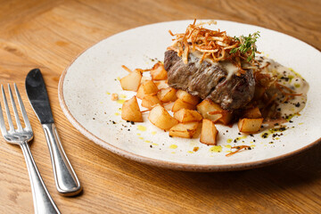 Grilled steak with baked golden potatoes served with crispy onion on top on a brick background....