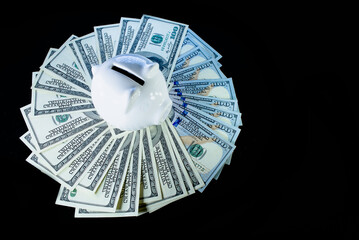 One hundred dollars bills in large quantities and a white piggy bank in the center on a black background