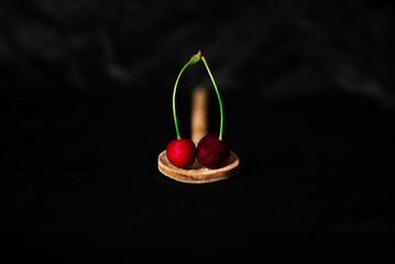 Two freshly picked cherries stand on a wooden spoon, on a dark background. Minimalistic concept....