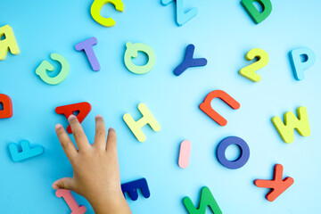 The wooden letters of the alphabet are colorful with the baby’s hand reaching for the wooden...