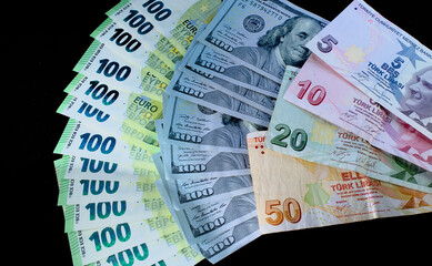 One hundred dollars, euros and Turkish lira banknotes in large quantities fanned out on a black background.