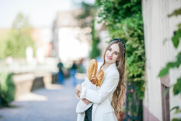 Young beautiful long-haired woman 25 years old in a black and white dress buys a French baguette in...