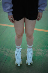 Legs of a young woman wearing white roller skates. She is at a soccer field. High angle shot.