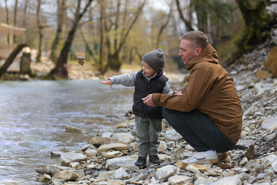 father and son spending time together in nature, throwing stones into the river, father's day, family, toddler, little boy, fatherhood, outdoor activities with parents, forest river, baby and daddy