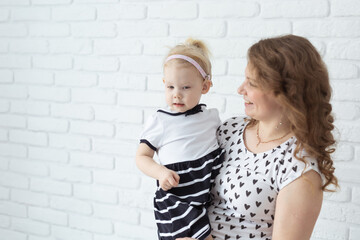 Mother holds and having fun her child with hearing aids and cochlear implants on white brick wall with copy space and place for advertising . Deaf and innovating medicine technologies concept