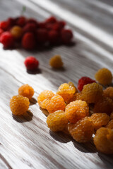 Two handfuls of fresh red and yellow raspberry on white wooden table.