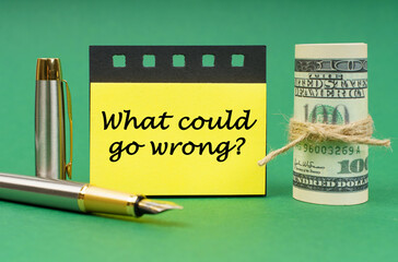 On a green surface, a pen, dollars, a notepad and yellow stickers with the inscription - what could go wrong
