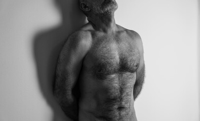 Monochrome of body of hairy adult man against white wall