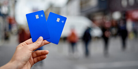 Two bank cards in the hand of a young girl against the background of a blurred street. Universal...