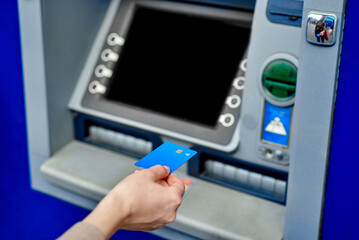 The girl's hand inserts the bank card into the ATM. Blue bank card. A woman uses an ATM on the...