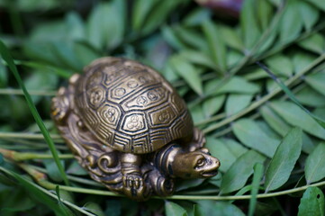 Turtle figurine close-up on a background of green leaves.