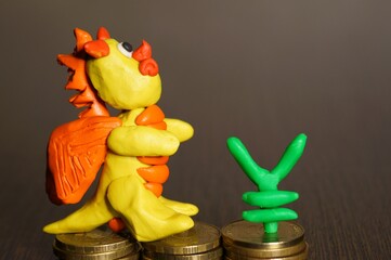 A toy dragon made of plasticine with coins and a figure of yen. Financial symbol.